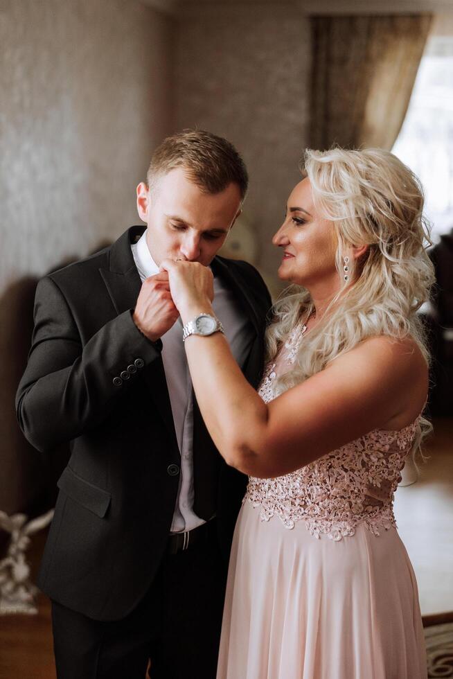 mãe ajuda dela adulto filho preparar para a Casamento cerimônia. a emocional e tocante momento às uma casamento. uma mãe abraços dela filho foto