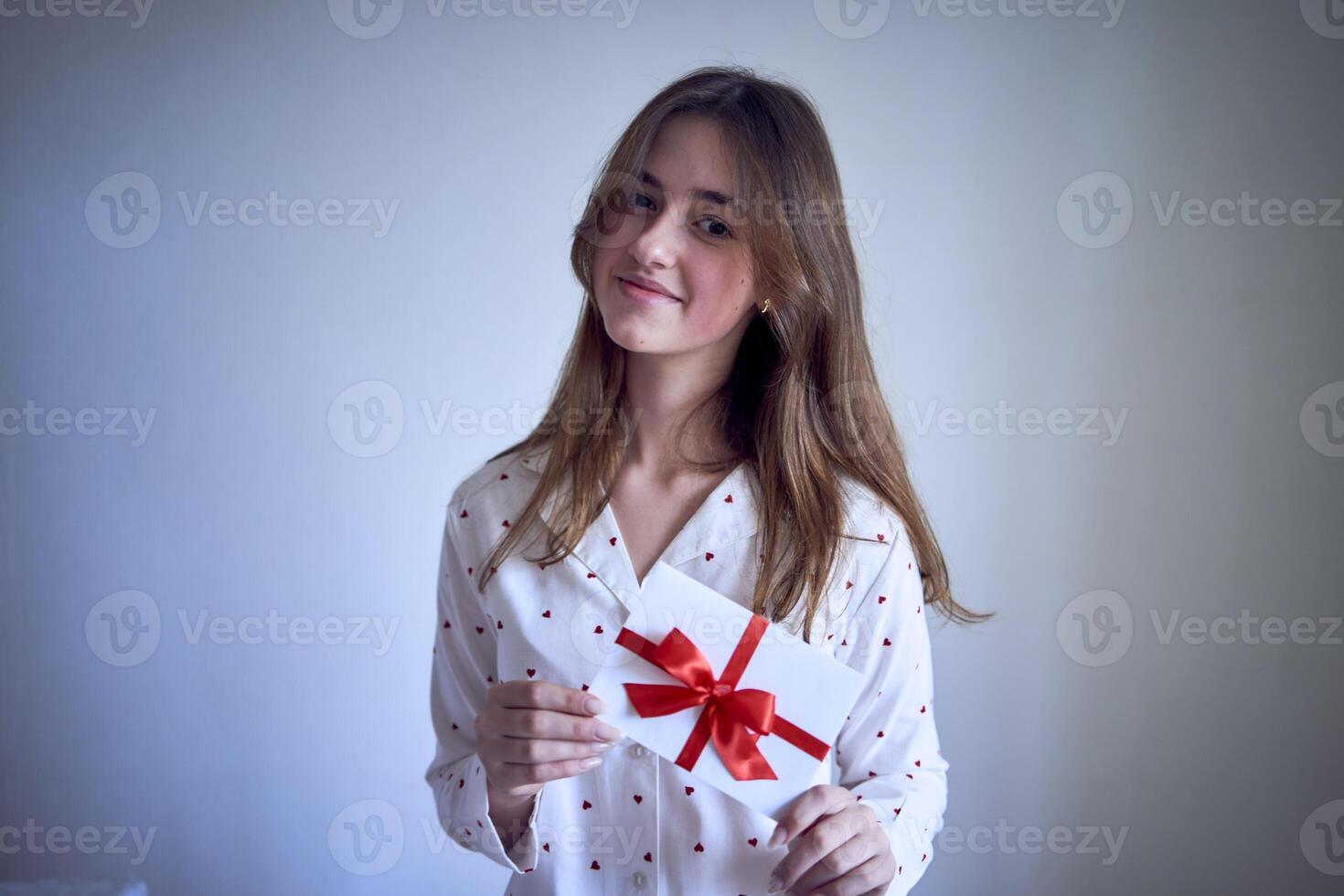 presente certificado dentro a mãos do uma Adolescência menina vestindo branco pijamas com vermelho corações foto