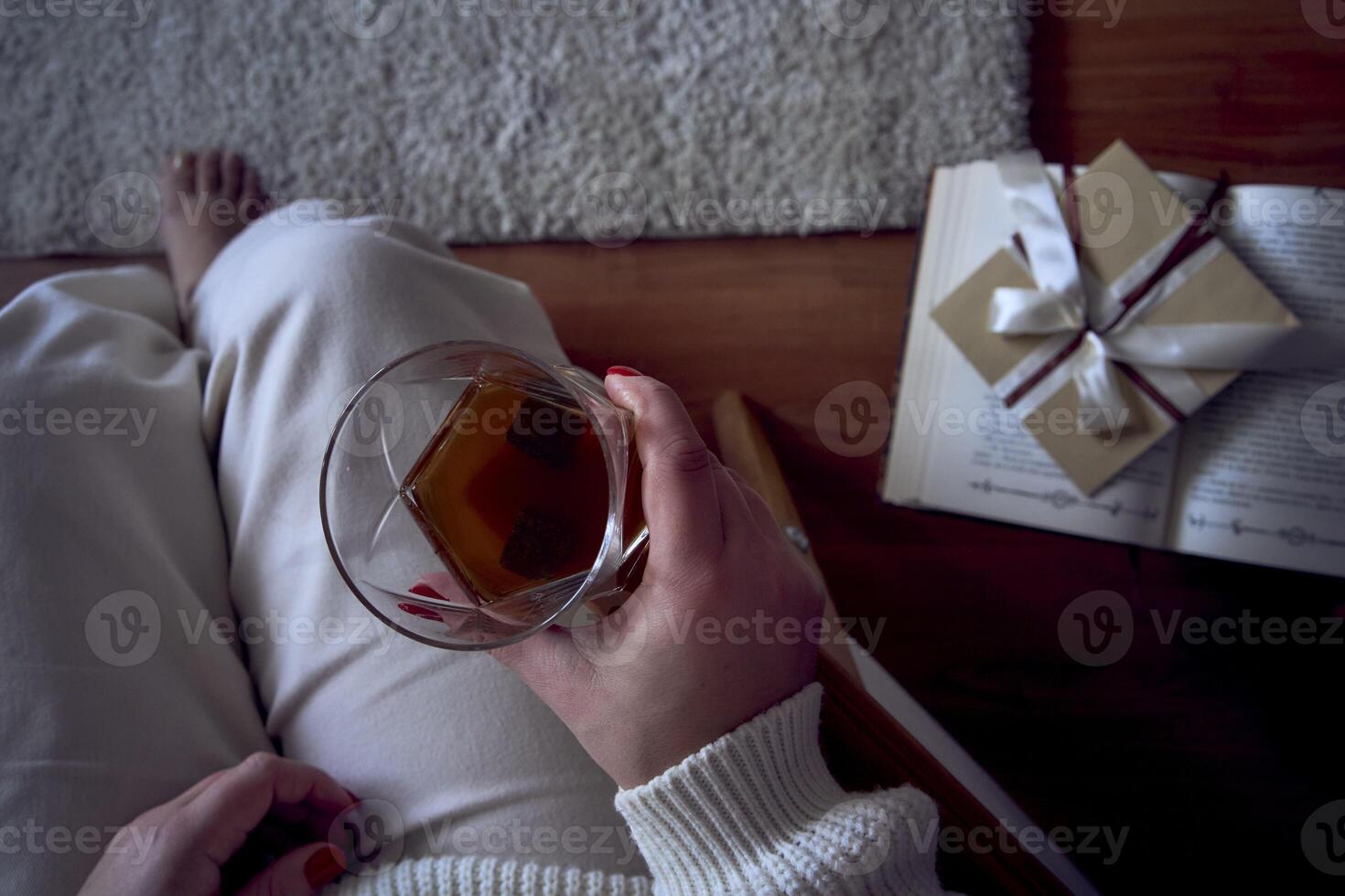 uma tamanho médio mulher senta dentro a poltrona lendo uma livro e bebendo uísque, uma presente certificado é Próximo para dela foto