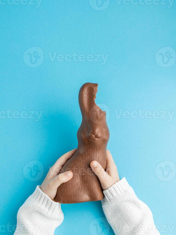 criança segurando chocolate Páscoa Coelho com orelhas mordido fora em azul fundo foto