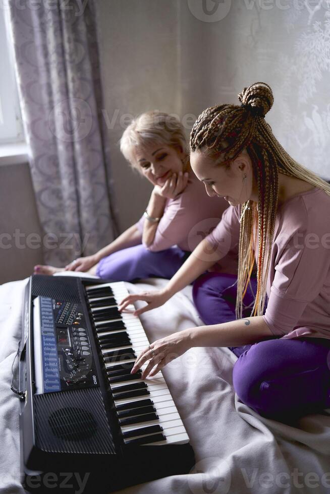 uma 60 anos mãe e uma 40 anos filha jogar a teclado juntos em a cama às casa foto