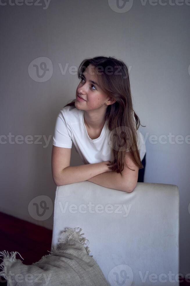 retrato do uma lindo Adolescência menina em uma cadeira dentro uma brilhante quarto dentro uma minimalista estilo foto