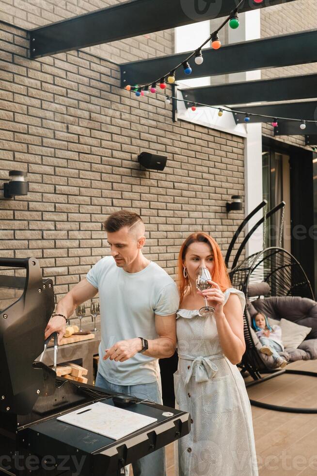 uma casado casal cozinheiros grelhado carne juntos em seus terraço foto