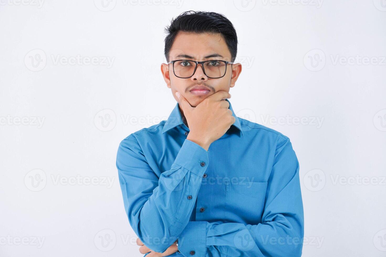 pensando ásia homem de negocios com óculos segurando uma queixo vestindo azul camisa isolado em branco fundo foto