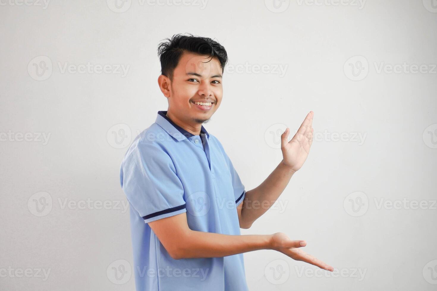 sorridente ásia homem aberto braços apontando para a lados vestindo azul t camisa isolado em branco fundo foto