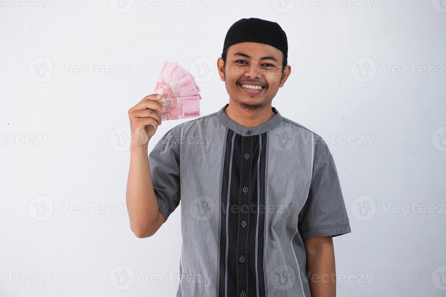 sorridente ou feliz jovem ásia muçulmano homem segurando papel dinheiro presente thr a partir de família Ramadã eid al-fitr Tempo vestindo cinzento muçulmano roupas isolado em branco fundo foto