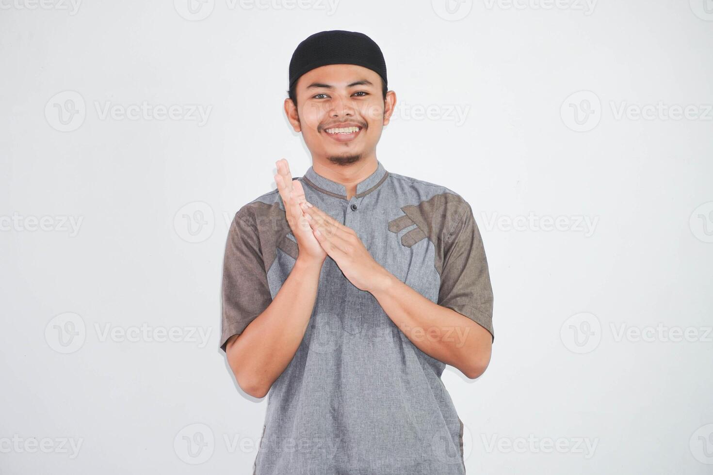 sorridente jovem ásia muçulmano homem palmas dentro mãos e olhando às Câmera vestindo cinzento Koko roupas isolado em branco fundo foto