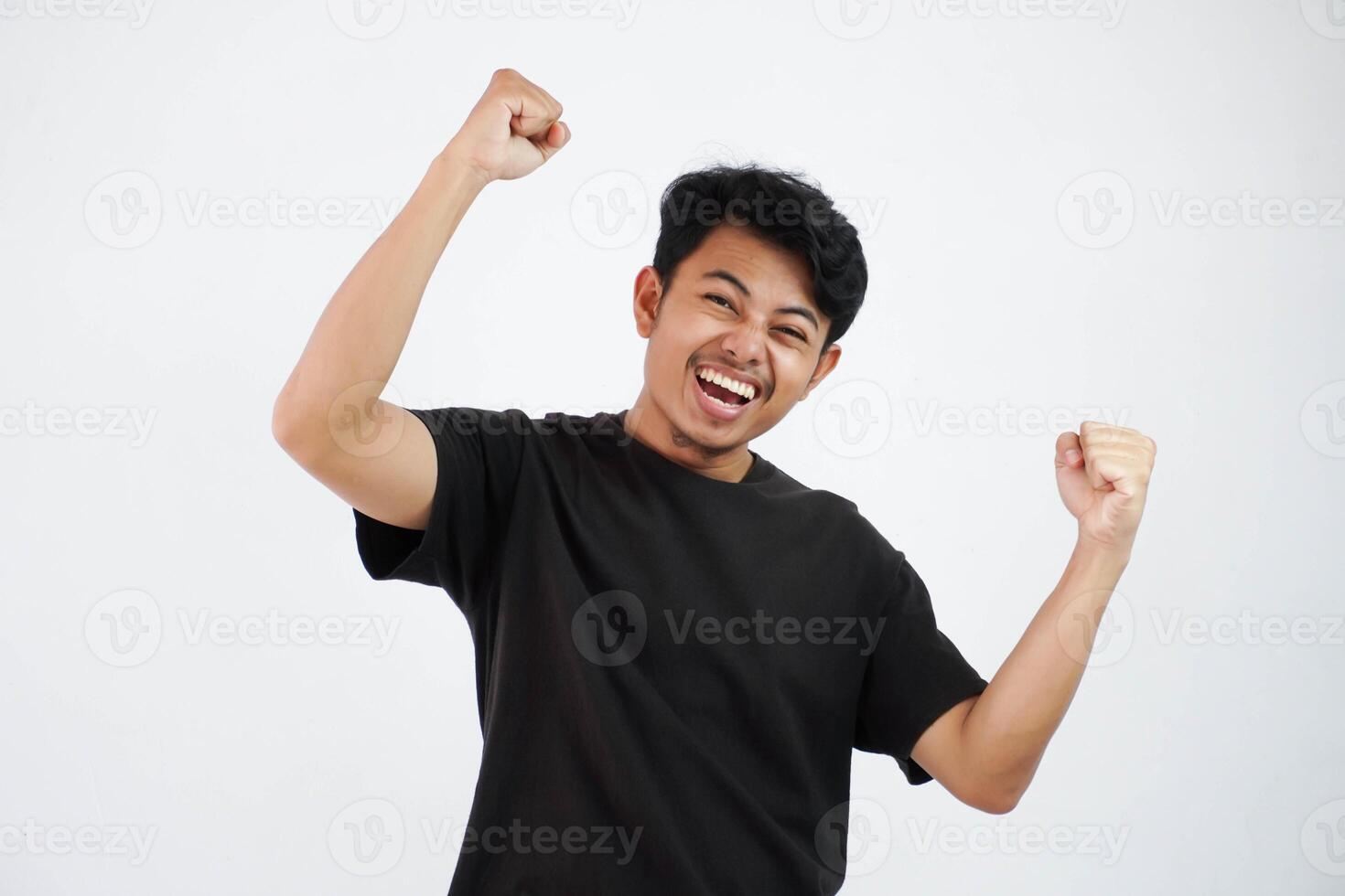 confiante alegre bonito ásia homem elevação mãos acima vestindo Preto t camisa vencedora gesto aperto punhos. sente felicidade mostrar punho acima sucesso isolado em branco fundo foto