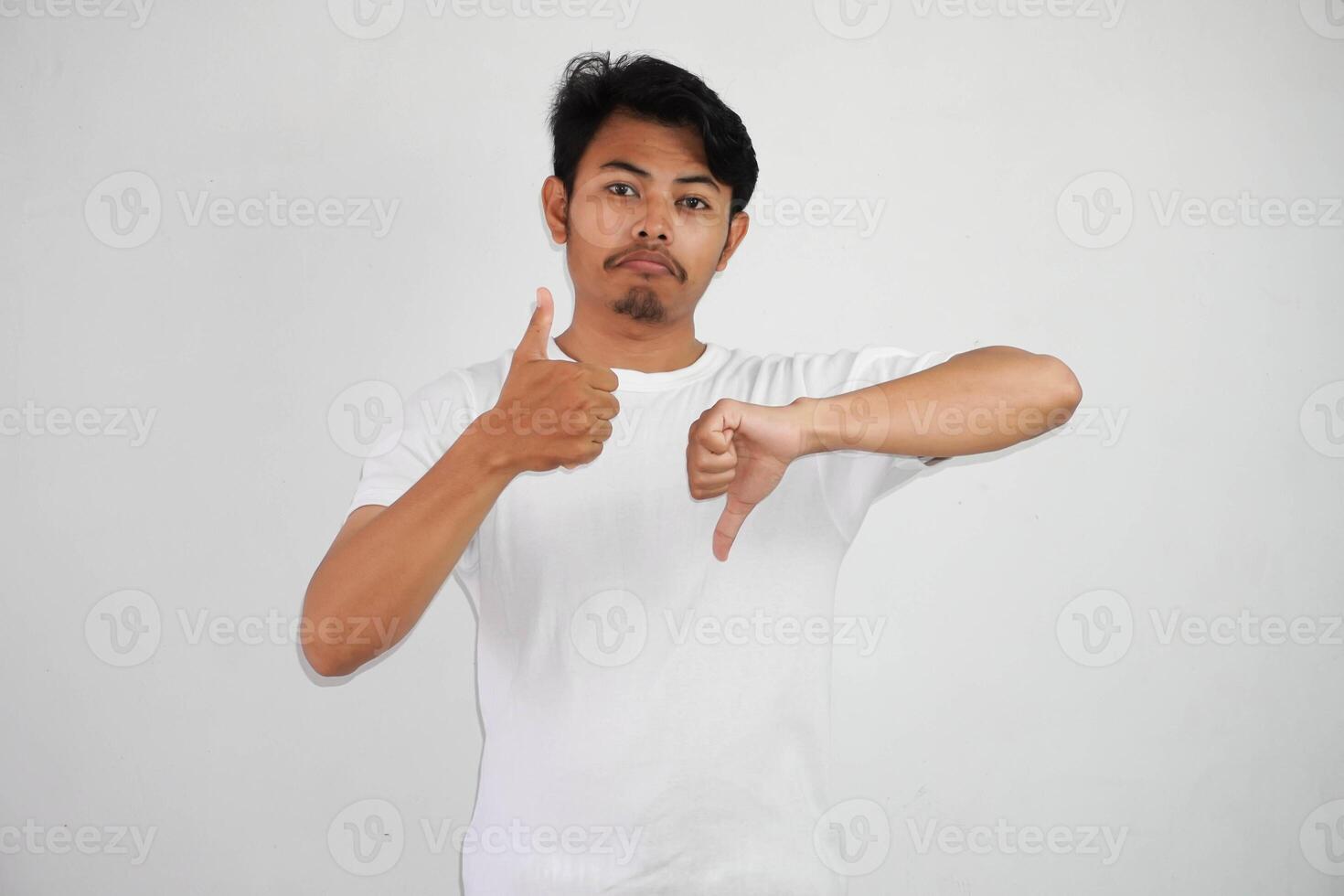 sério jovem ásia homem mostrando polegares acima e baixa decisão vestindo branco fundo isolado em branco fundo foto