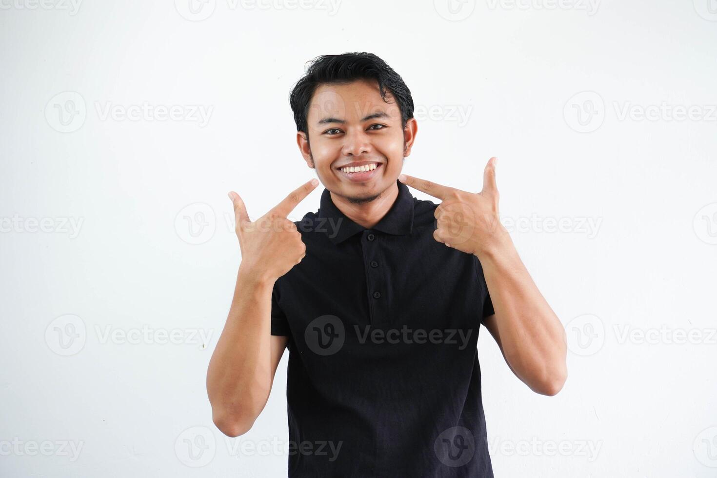 sorridente jovem ásia homem apontando para dele boca com feliz expressão vestindo Preto pólo t camisa isolado em branco fundo foto