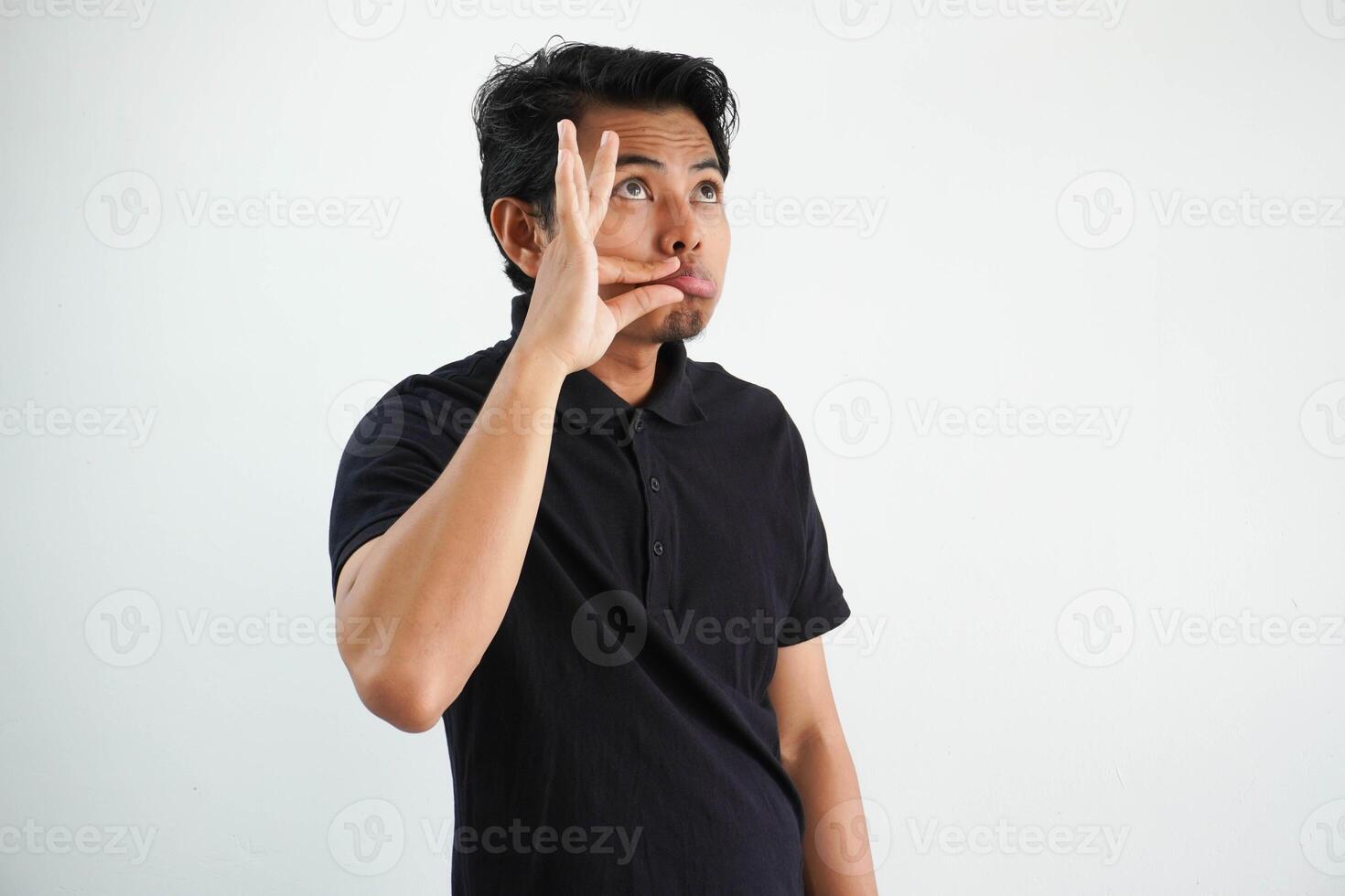 jovem ásia homem fechar dele boca acima com sério expressão, com dedos em lábios guardando uma segredo. vestindo Preto pólo t camisa isolado em branco fundo foto