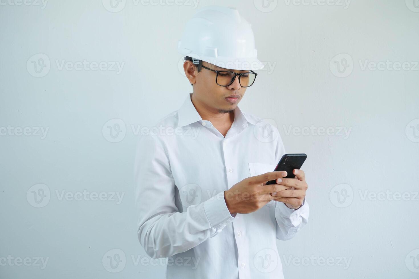 jovem ásia masculino arquiteto engenheiro sério enquanto olhando às a celular isolado em branco fundo. foto