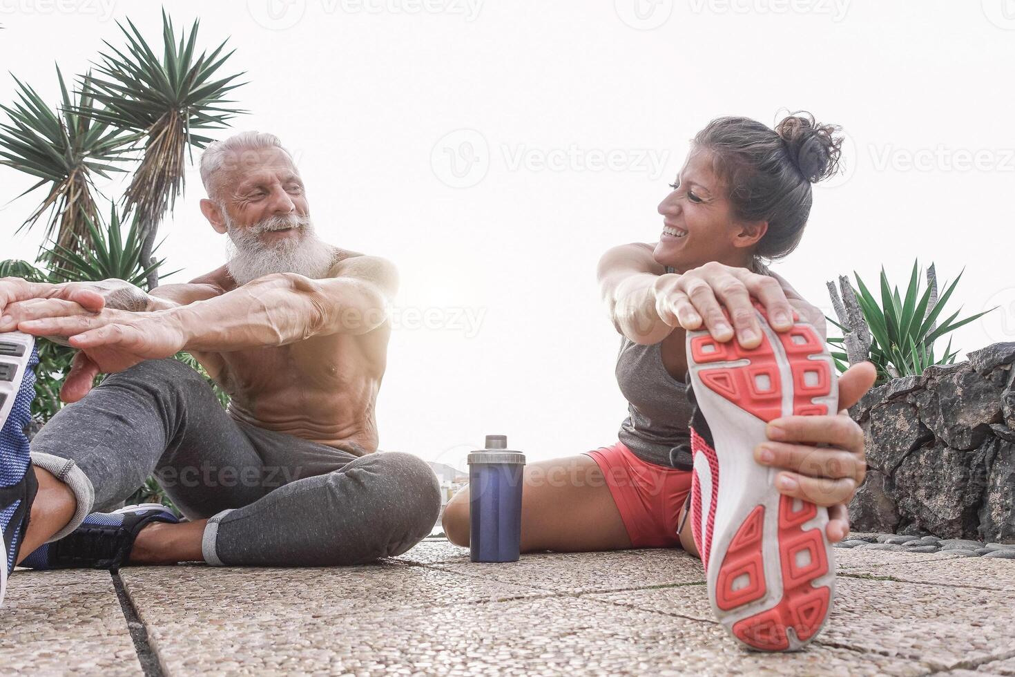 feliz ginástica amigos fazendo pernas alongamento exercícios juntos dentro ao ar livre área - desportivo casal exercite-se enquanto rindo olhando cada de outros durante uma ensolarado dia - ginástica e esporte estilo de vida conceito foto