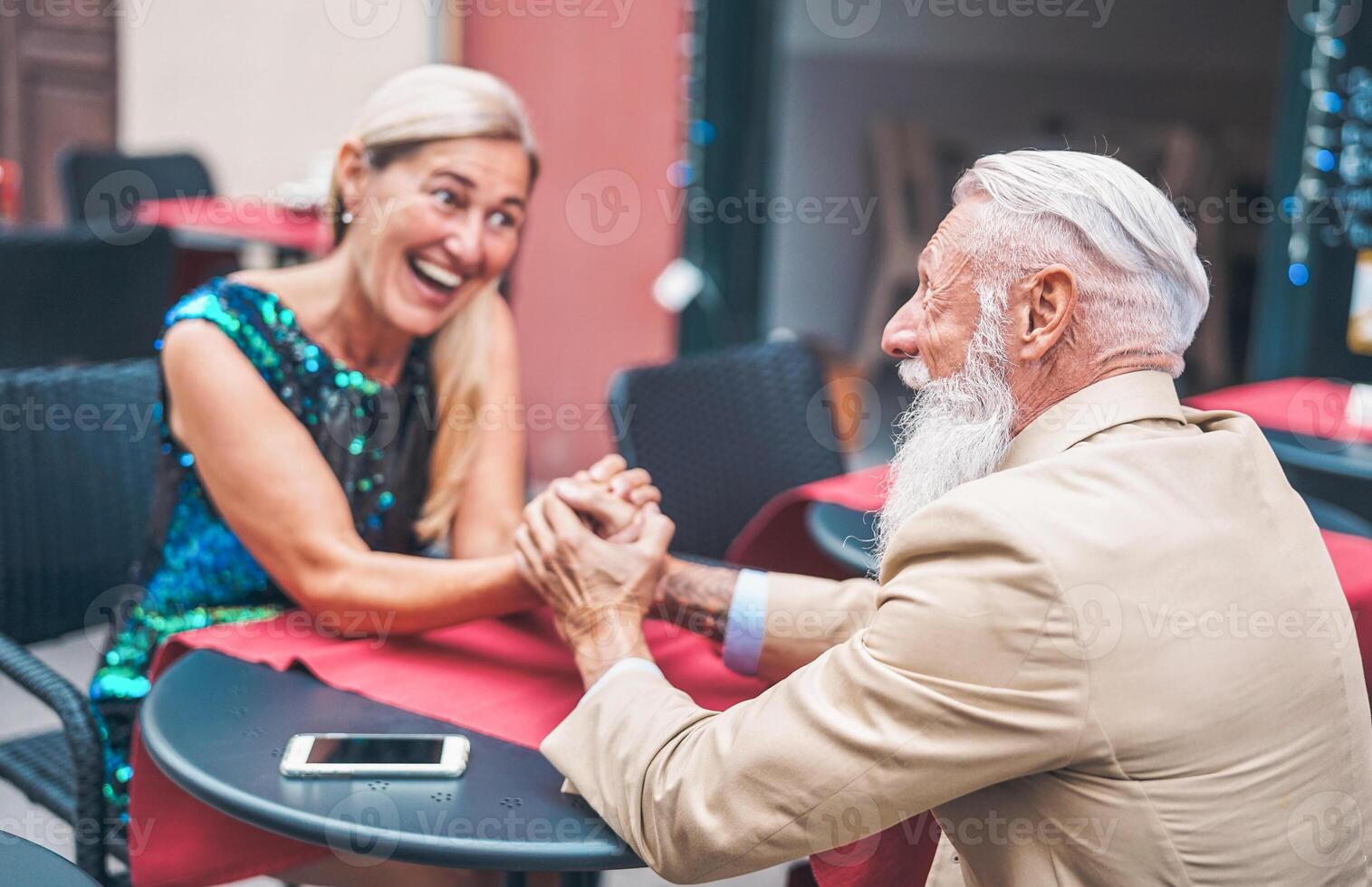 feliz Senior casal segurando mãos enquanto sentado dentro uma Barra ao ar livre - elegante maduro marido e esposa olhando cada de outros enquanto relaxante dentro uma restaurante - pessoas, felicidade, amor e casamento conceito foto
