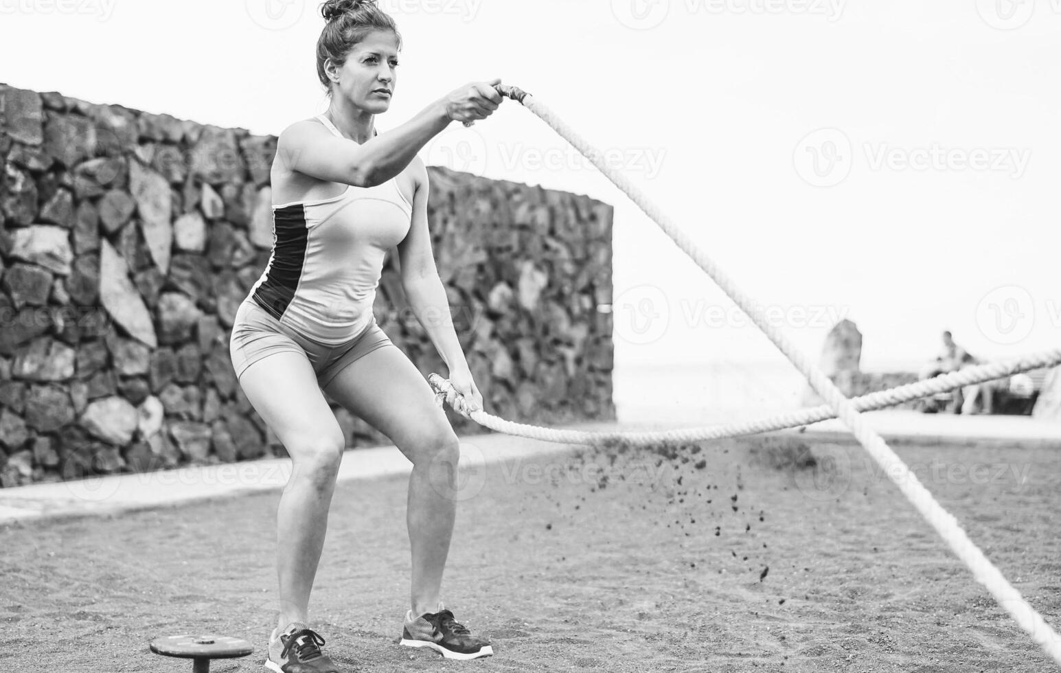 em forma mulher Treinamento com batalha corda ao ar livre - fêmea atleta fazendo braços exercícios em a de praia - corpo construção e esporte estilo de vida conceito - Preto e branco editar foto