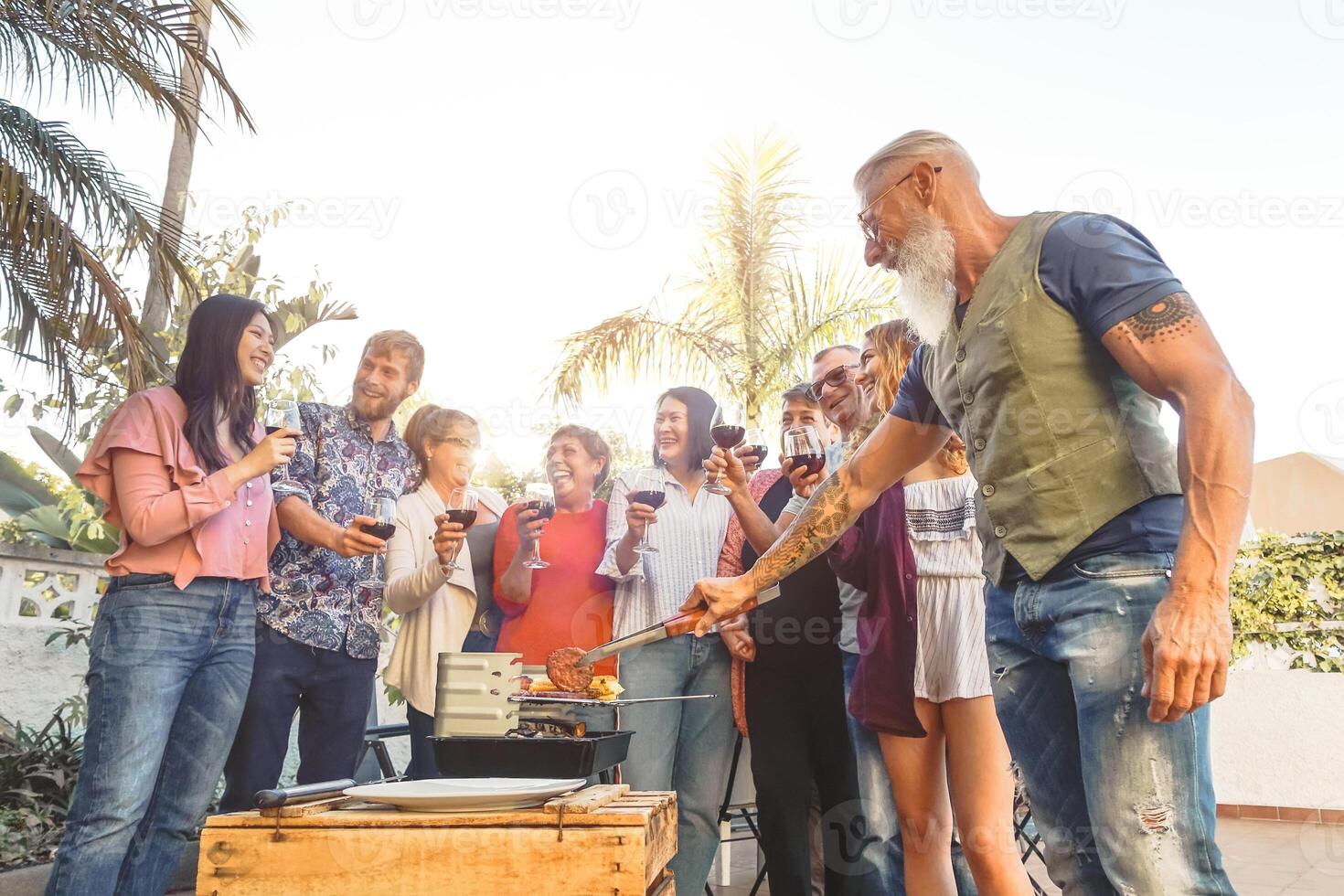 feliz família bebendo vermelho vinho dentro churrasco festa - chefe de cozinha Senior homem grelhar carne e tendo Diversão com pais - final de semana Comida churrasco e reunião jovem e Mais velho pessoas estilo de vida conceito foto