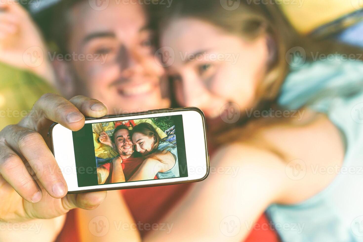 jovem casal do amantes levando deitado em Relva levando uma selfie com Móvel telefone - feliz adolescentes dentro amor fazer uma auto retrato usando Smartphone Câmera - caloroso vintage filtro - foto