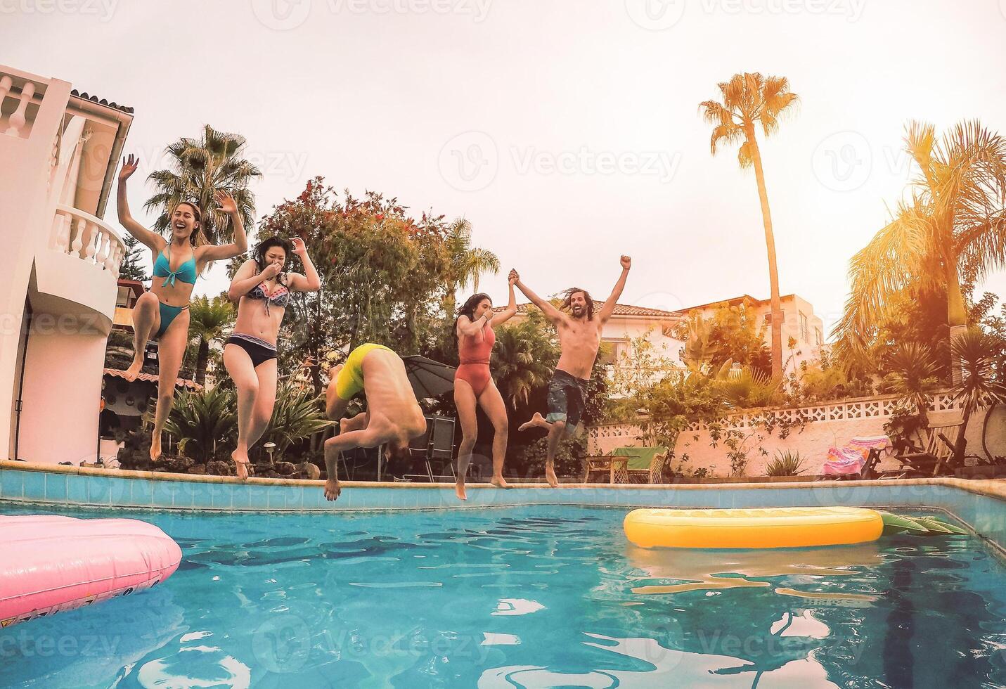 grupo do feliz amigos pulando dentro piscina às pôr do sol Tempo - milenar jovem pessoas tendo Diversão fazer festa dentro exclusivo recorrer tropical - feriados, verão, período de férias e juventude estilo de vida conceito foto