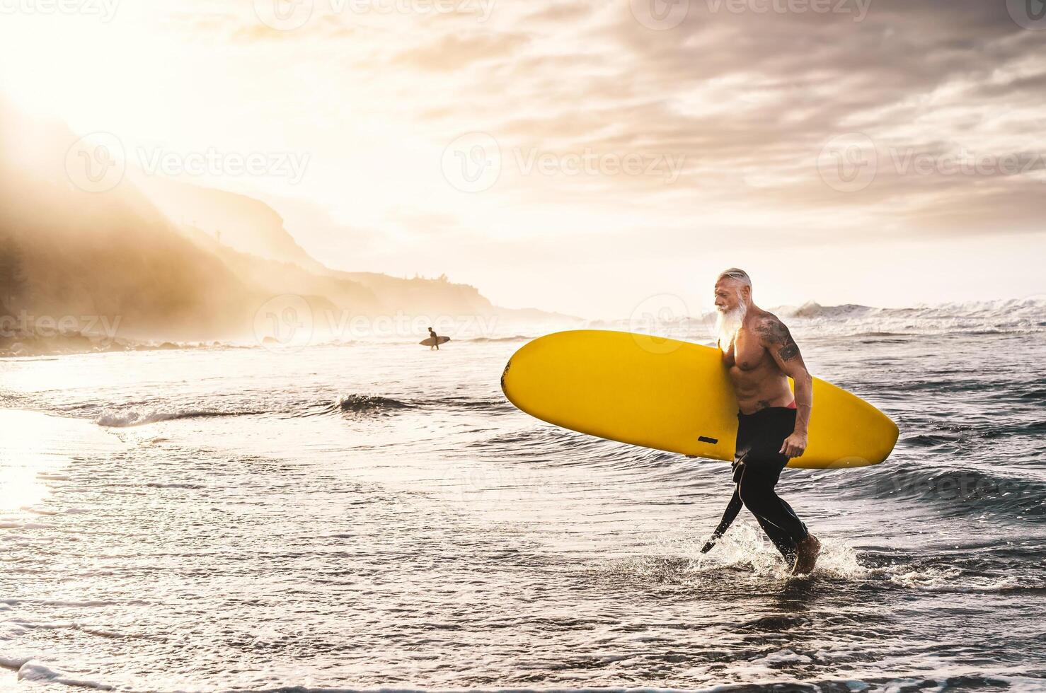 feliz em forma Senior surfar em pôr do sol Tempo - desportivo maduro homem tendo Diversão Treinamento com prancha de surfe dentro oceano - idosos saudável pessoas estilo de vida e extremo esporte conceito foto