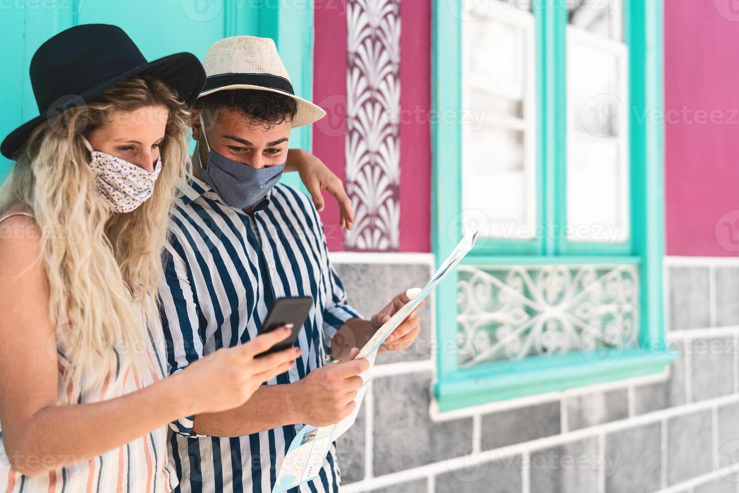 jovem casal vestindo face protetora mascarar enquanto usando Móvel telefone e segurando viagem mapa - Viajantes pessoas desfrutando primeiro viagem depois de corona vírus surto - viagem saúde e tecnologia conceito foto