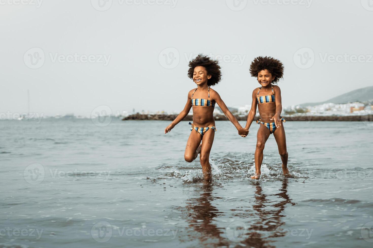 feliz irmãs corrida juntos dentro água durante verão Tempo - afro crianças tendo Diversão jogando em a de praia - família amor e viagem período de férias estilo de vida conceito foto