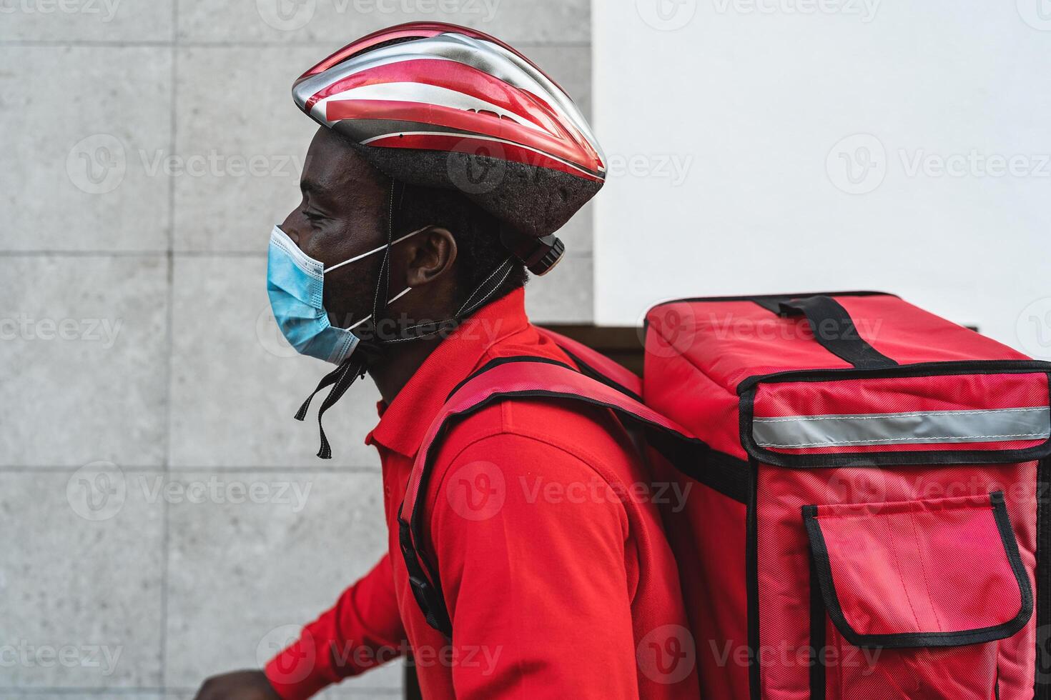 africano cavaleiro homem entregando refeição para clientes com elétrico bicicleta enquanto vestindo face mascarar durante corona vírus surto - eco velozes Entrega Comida conceito foto