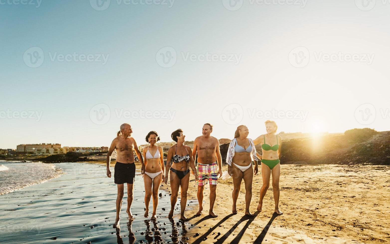 feliz multirracial Senior amigos tendo Diversão caminhando em a de praia às pôr do sol durante verão feriados - diverso idosos pessoas desfrutando Férias foto