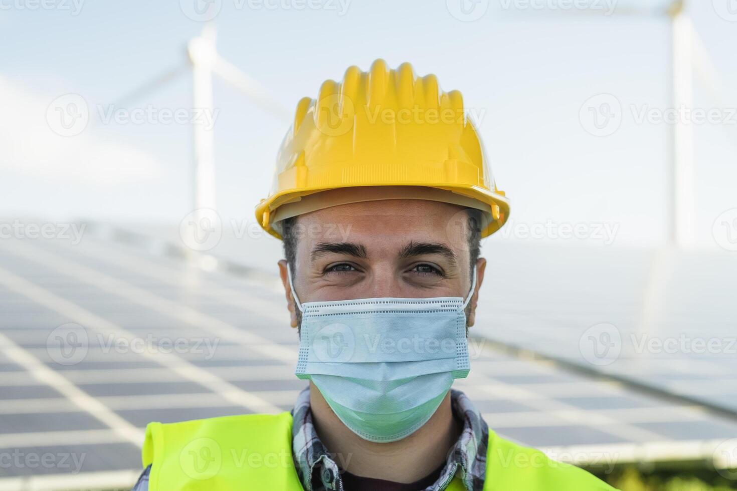 jovem engenheiro trabalhando para alternativo energia com vento turbina e solar painel enquanto vestindo face mascarar durante corona vírus surto - inovação e verde poder conceito foto