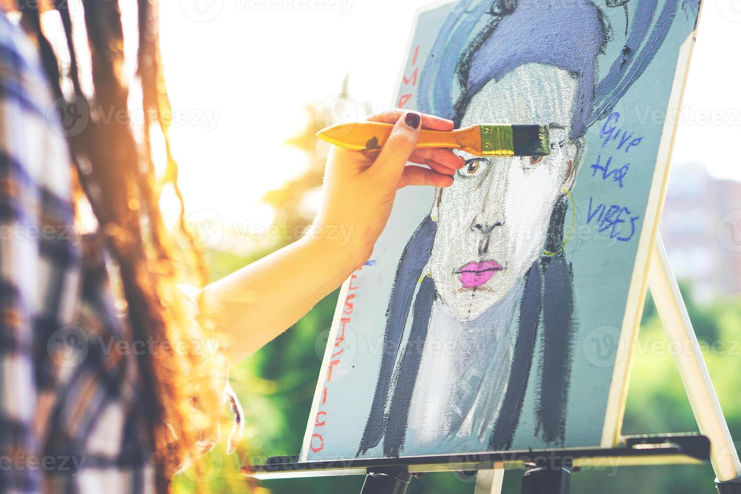 jovem artista pintura uma auto retrato dentro uma parque ao ar livre - fechar acima do pintor com tranças Penteado trabalhando em dela arte dentro a cidade às pôr do sol - conceito do pessoas expressando artes - foco em pintura foto