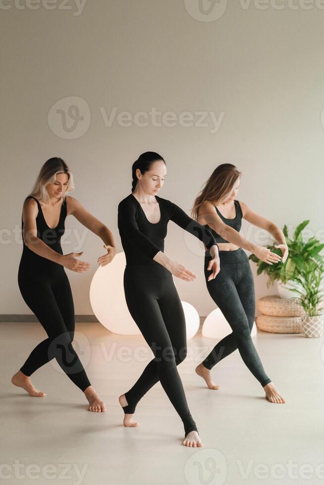 uma grupo do meninas dentro Preto fazendo ioga poses dentro de casa. mulheres estão acionado dentro ginástica foto