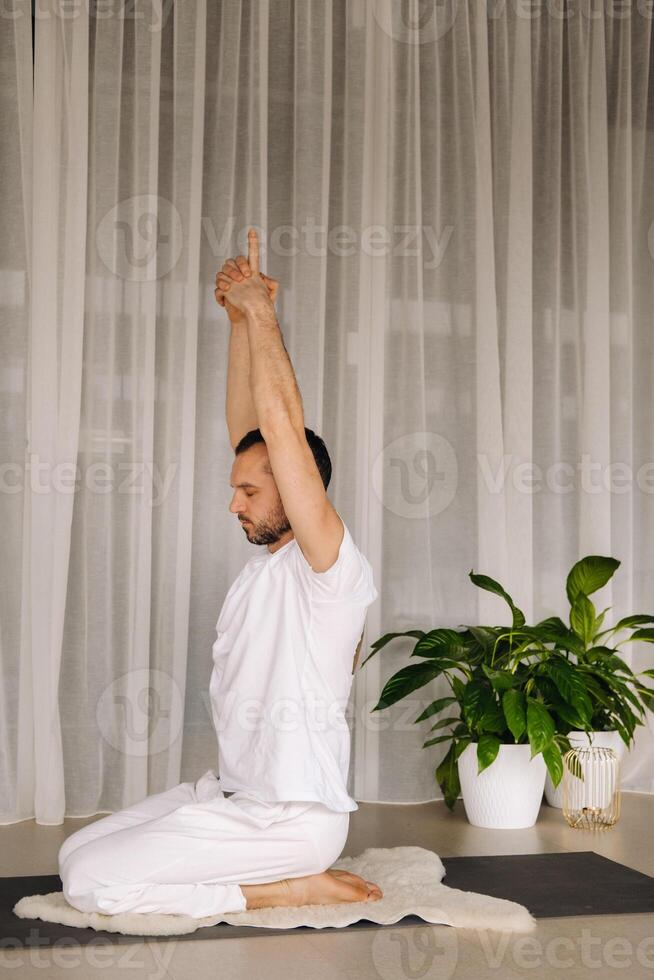 uma homem dentro branco roupa de esporte é fazendo ioga com uma ginástica sala. a conceito do uma saudável estilo de vida foto