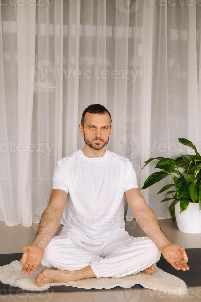 uma homem dentro branco roupa de esporte é fazendo ioga com uma ginástica sala. a conceito do uma saudável estilo de vida foto