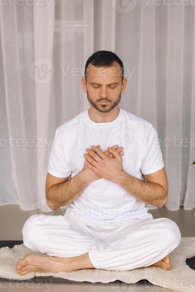 uma homem dentro branco roupa de esporte é fazendo ioga com uma ginástica sala. a conceito do uma saudável estilo de vida foto