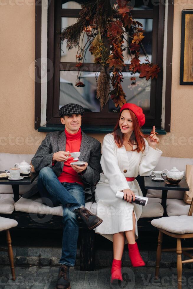 uma feliz à moda casal bebidas café e sorrisos enquanto sentado dentro uma cafeteria em a rua foto