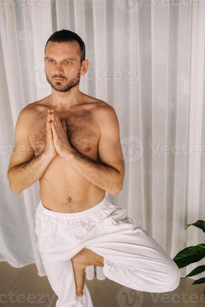 uma homem com uma nu tronco faz ioga dentro uma ginástica sala. a conceito do uma saudável estilo de vida foto