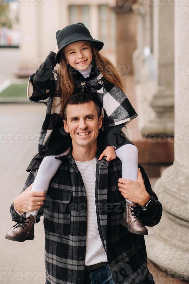 uma alegre filha é sentado em do pai ombros e caminhando por aí a outono cidade foto