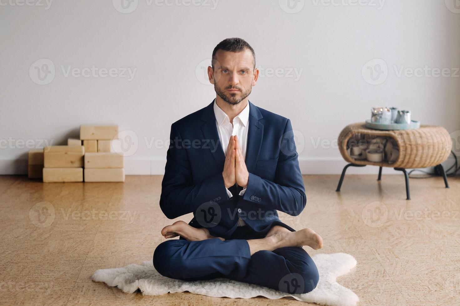 uma homem dentro uma rigoroso terno faz ioga enquanto sentado dentro uma ginástica quarto foto