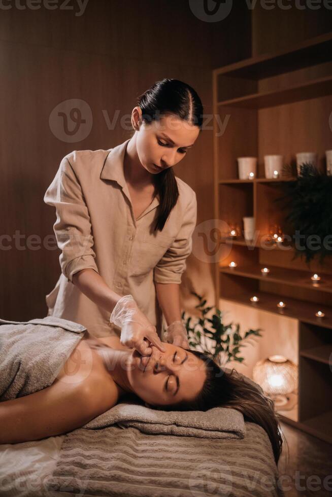 uma cosmetologista menina faz uma facial e pescoço massagem para uma menina dentro a escritório para pele elasticidade foto