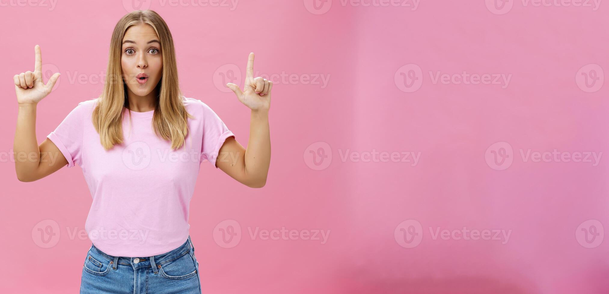 divertido e impressionado atraente comum europeu mulher com justo cabelo e bronzeada pele levantando índice dedos apontando acima espantado dobrando lábios a partir de interesse e espanto sobre Rosa fundo foto