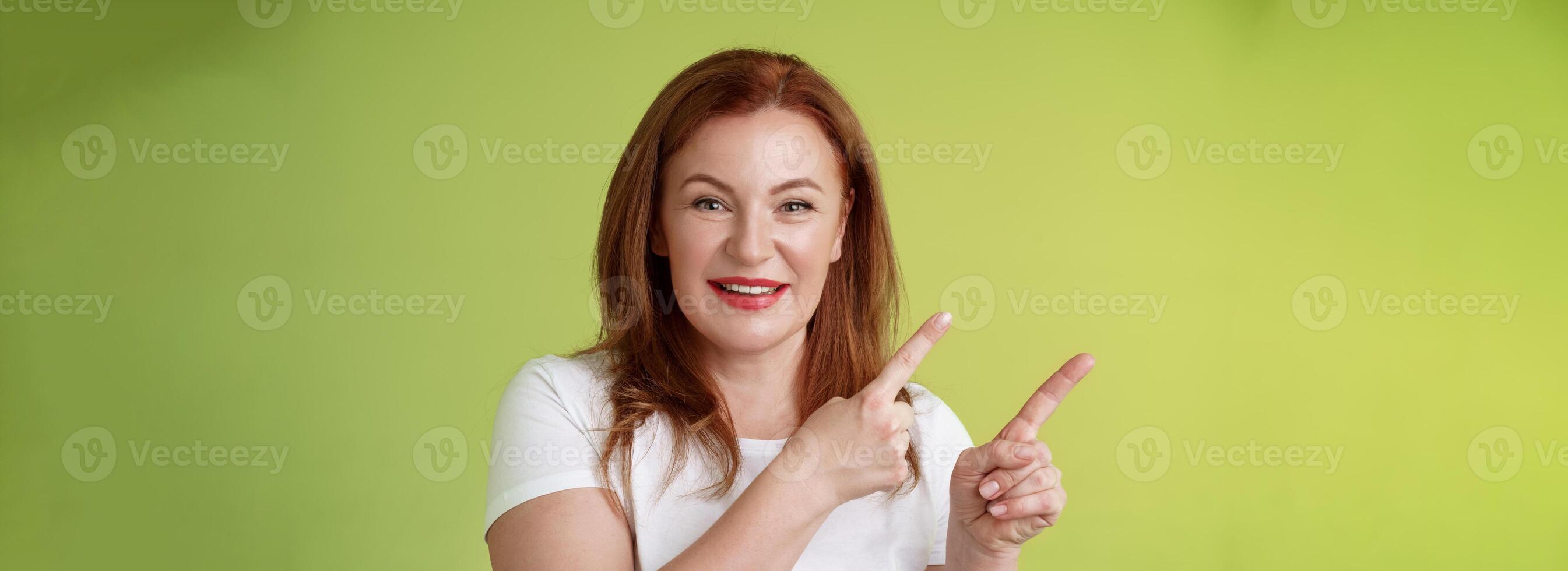 fechar-se alegre motivado agradável ruiva meia idade fêmea apontando superior esquerda canto índice dedos sorridente Deleitado dar adendo Confira promo Boa propaganda em branco espaço verde fundo foto