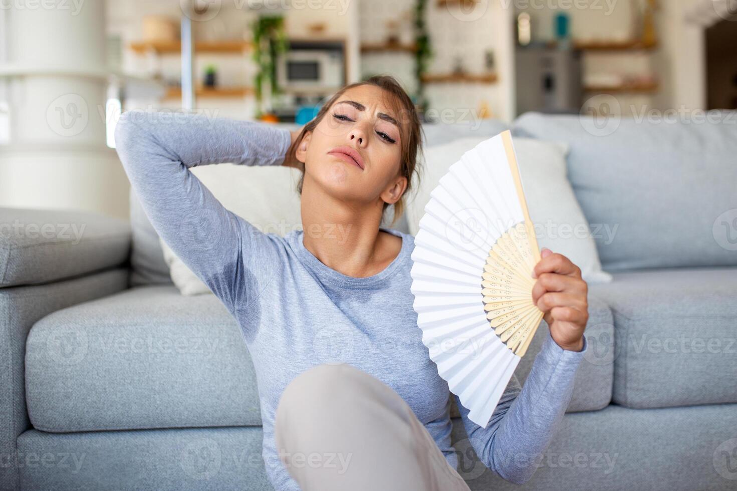 mulher acenando uma fã, batalhas superaquecimento e verão calor às lar. dela saúde e hormônios estão afetado, drenado de exaustão vencimento para a falta do ar condicionamento. a conceito do insolação foto