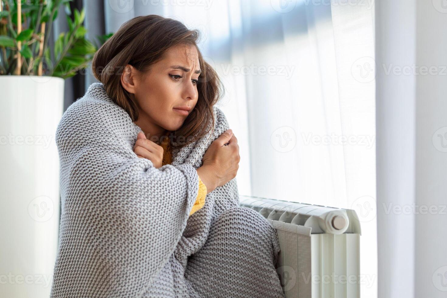 indisposto mulher locatário dentro cobertor sentar dentro frio vivo quarto mão em velho radiador.sofrer a partir de falta do calor . pouco saudável jovem mulher luta a partir de calafrio congelar às lar. não aquecimento conceito. foto