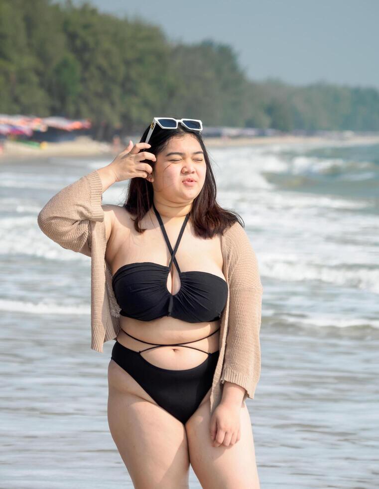 retrato jovem ásia mulher gordo gordo fofa lindo sorrir feliz Diversão apreciar relaxar bikini roupa de banho corpo sexy frente Visão mar de praia branco areia limpar \ limpo céu azul calma natureza oceano onda água viagem em feriado foto