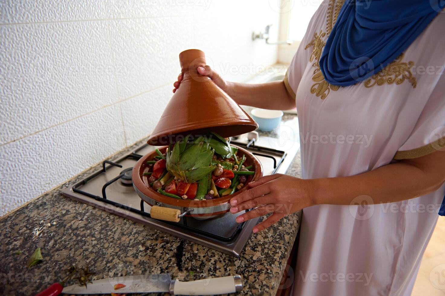 fechar-se meio Oriental dona de casa com cabeça coberto dentro hijab, em pé de forno, cozinhando marroquino tajine com legumes foto