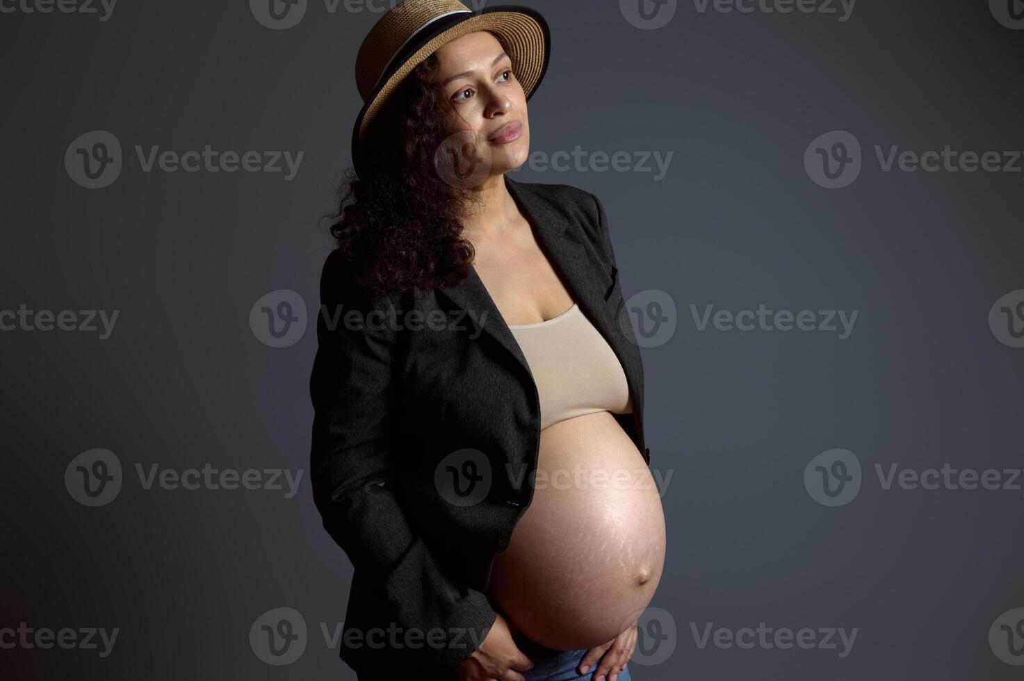 atraente pensativo jovem grávida mulher segurando dela barriga, sonhadoramente olhando a parte, de lado uma cópia de espaço em moda cinzento pano de fundo foto