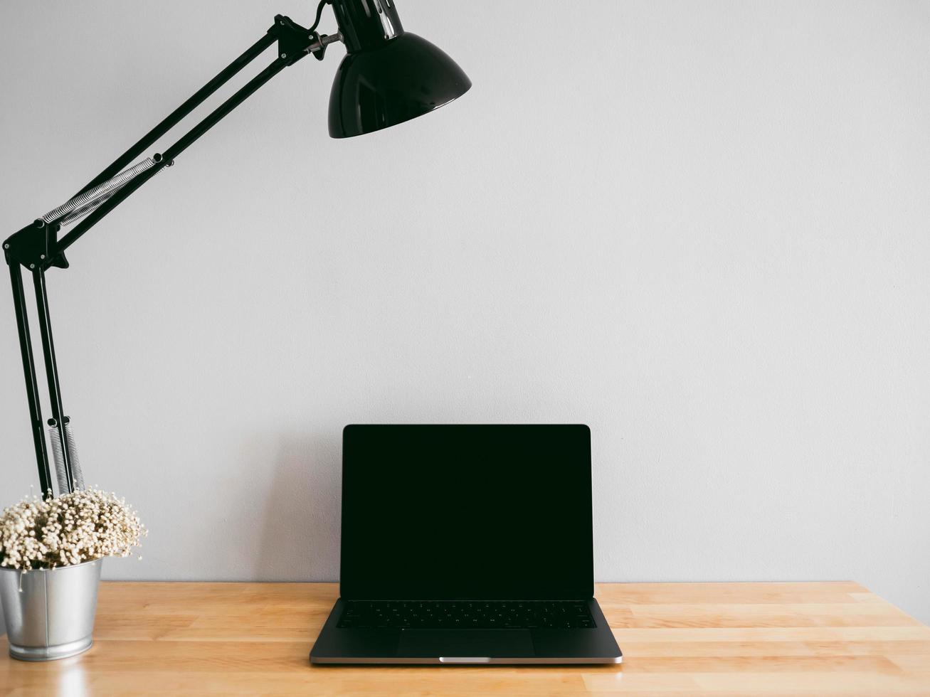 laptop e algumas ferramentas fixas na mesa de trabalho de madeira com uma parede cinza vazia como pano de fundo. conceito de espaço de trabalho e escritório mínimo. foto