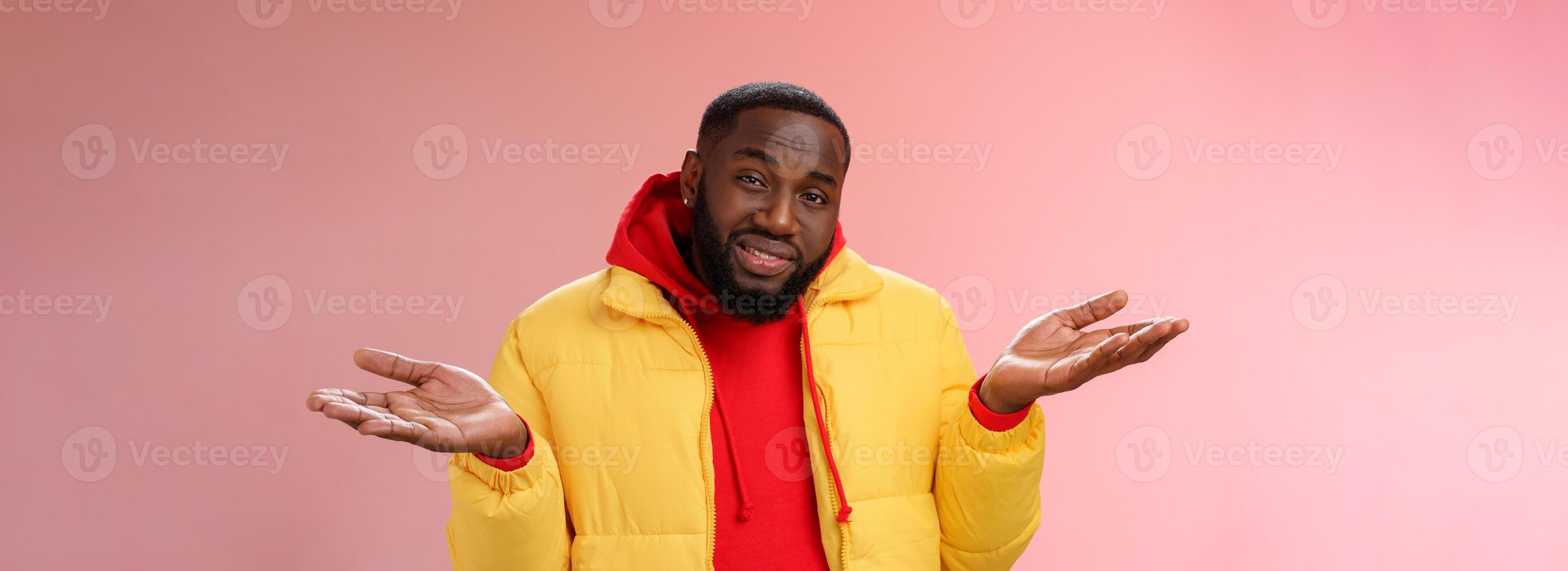 fechar-se sem noção inconsciente bonito à moda afro-americano barbudo homem dentro amarelo Jaqueta encolhendo os ombros mãos espalhar lateralmente desânimo não podes entender qualquer coisa em pé perplexo, Rosa fundo foto