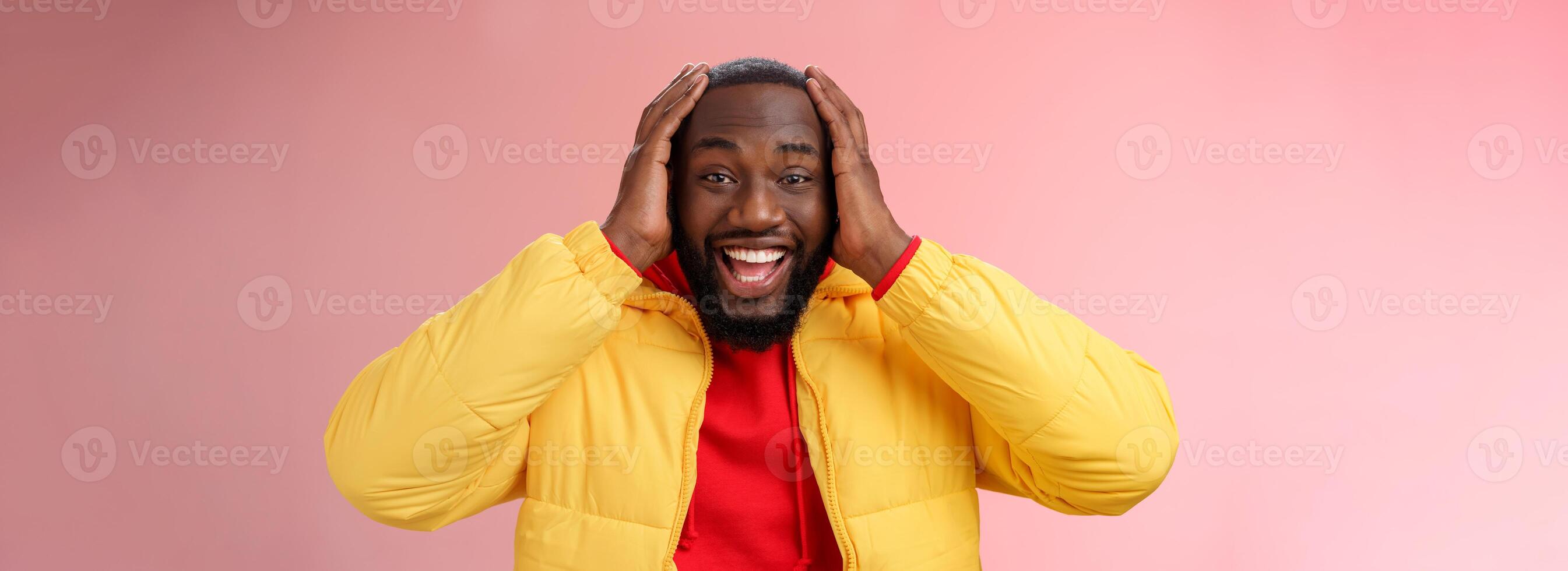 feliz surpreso satisfeito jovem afro-americano 25s homem jovem Jaqueta vermelho moletom com capuz sorridente divertido, atônito sorridente recebendo impressionante presente segurando mãos cabeça entusiasmado, em pé Rosa fundo foto