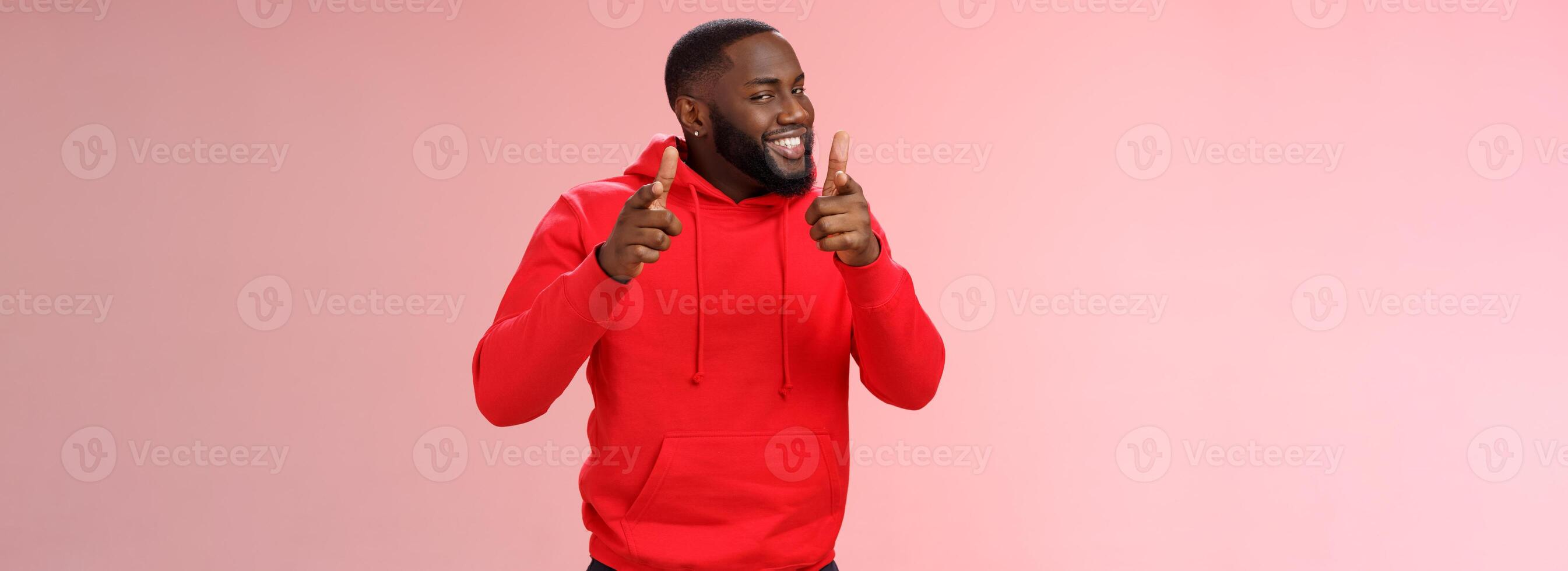 agradável trabalhos bem feito amigo. orgulhoso torcendo boa aparência atrevido jovem provocante Preto cara barba dentro vermelho moletom com capuz apontando dedo pistolas Câmera presunçoso parabenizando companheiro Boa jogo, em pé Rosa fundo foto