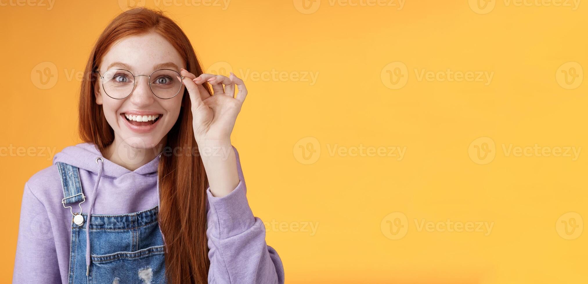 feliz entusiasmado jovem ruiva menina divertido encontrar Fora excelente Lugar, colocar comemoro aniversário em pé alegre animado toque óculos sorridente amplamente branco dentes sorrindo alegria surpreso, laranja fundo foto